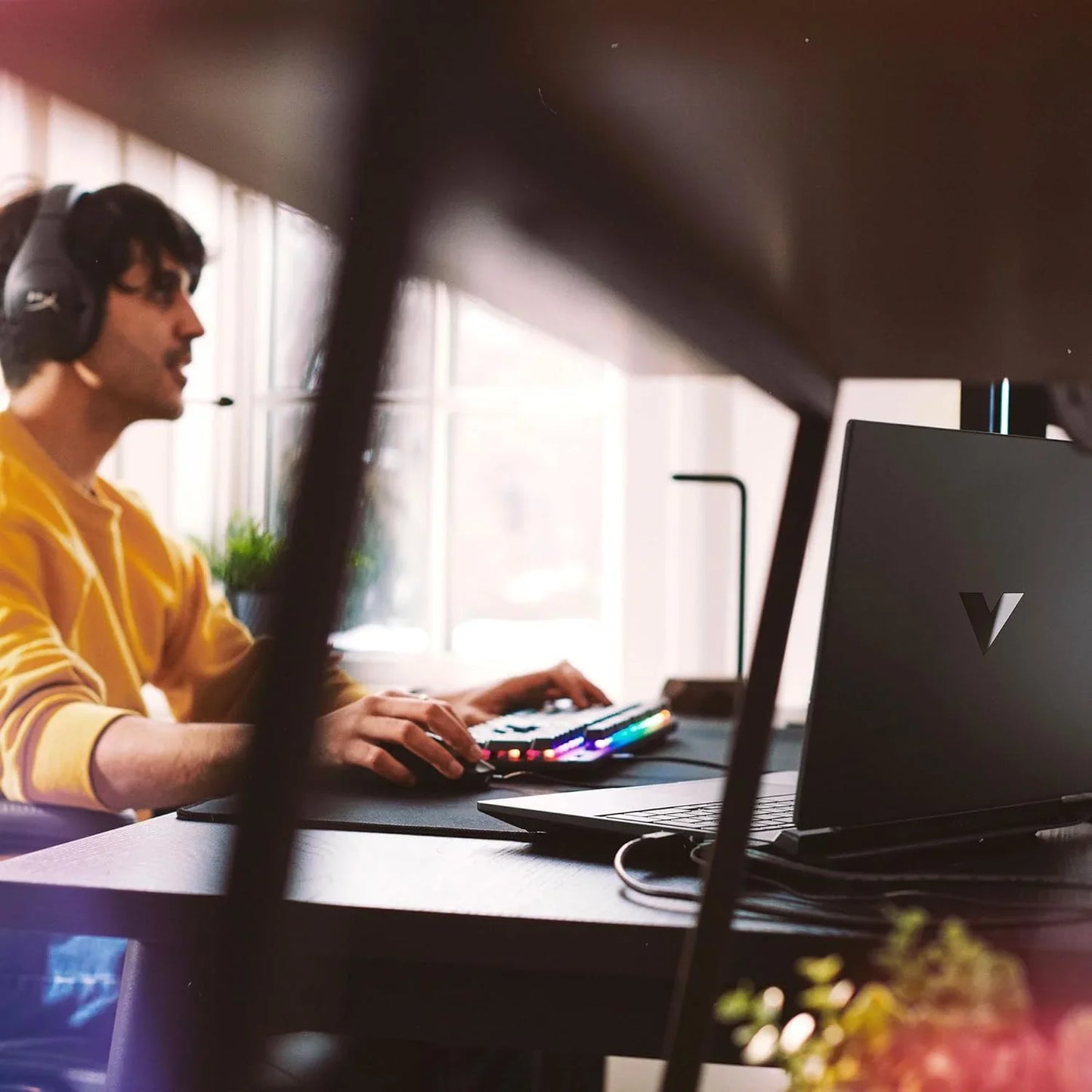 TechNest Victus 15.6 inch gaming laptop on desk with gamer using headset and RGB keyboard