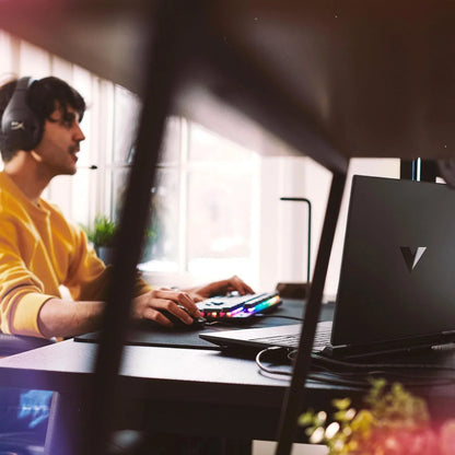 TechNest Victus 15.6 inch gaming laptop on desk with gamer using headset and RGB keyboard